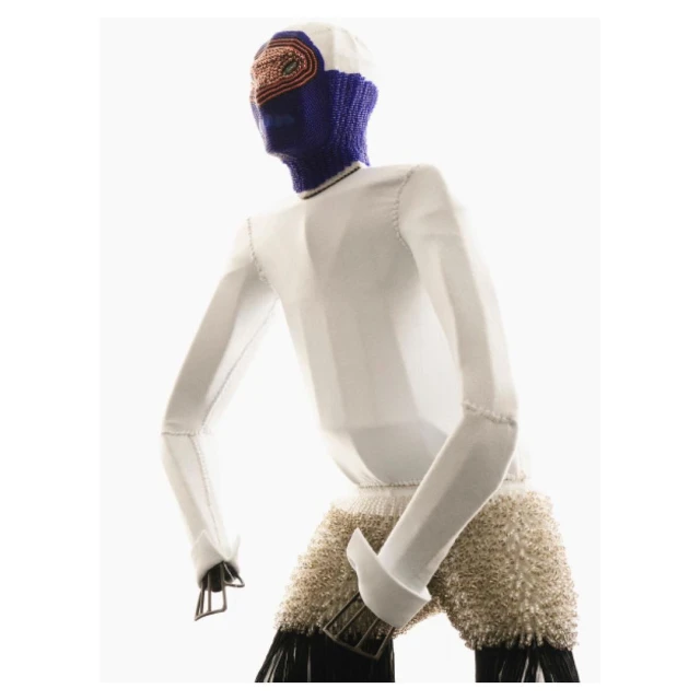Abstract person in a white jacket, textured shorts, and a balaclava with a colorful patterned headpiece posing against a white background.