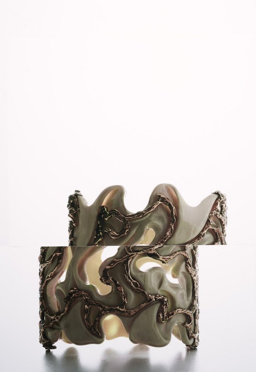Two decorative ceramic cuff bracelets with abstract gold-colored metallic designs stacked on a white surface in a studio setting.