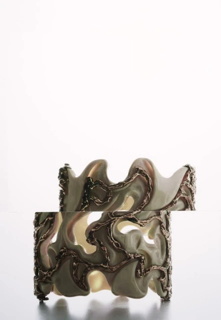 Two decorative ceramic cuff bracelets with abstract gold-colored metallic designs stacked on a white surface in a studio setting.