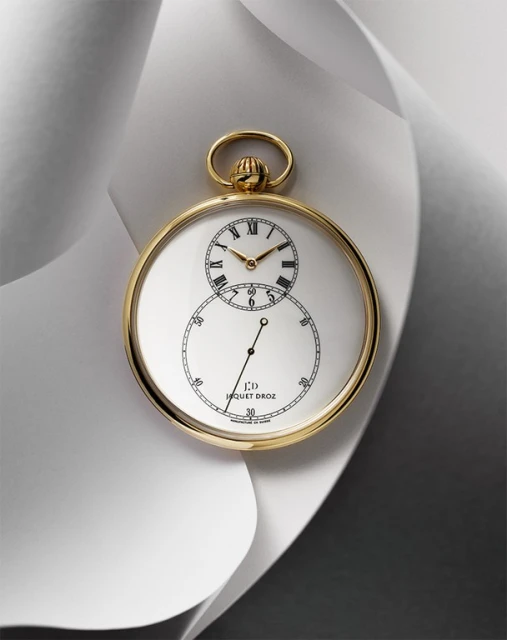 Elegant gold Jaquet Droz pocket watch with a white face displayed on a flowing white surface, showcasing luxury and classic design.