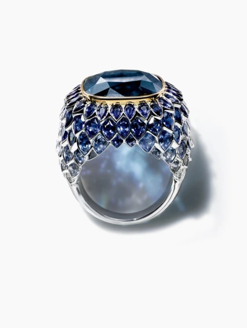 Cocktail ring featuring an oval, dark blue gemstone surrounded by rows of graduated blue gems set in a silver band on white.