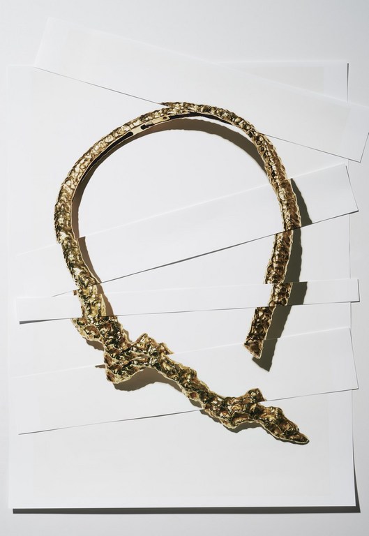 A gold collar necklace is artfully displayed against a background of layered white paper, highlighting its design and texture.