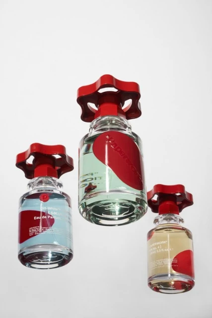 Three glass perfume bottles with red valve-shaped caps, featuring different colored liquids against a stark white background.