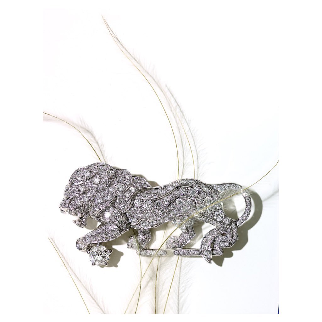 Diamond lion brooch resting among delicate white feathers against a clean white background