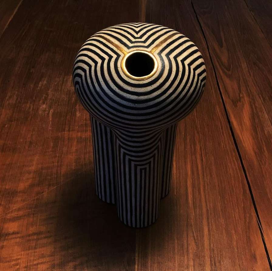 A black and white striped ceramic vase with three legs and a golden rim, standing on a dark brown wooden surface.
