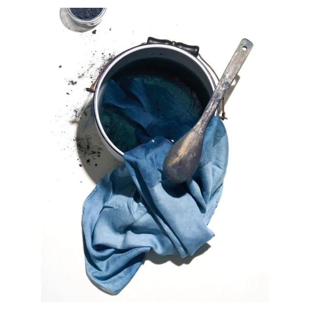 Still life of indigo dye ingredients: powder, liquid in a pot, cloth, and wooden spoon. Focus on color and texture.