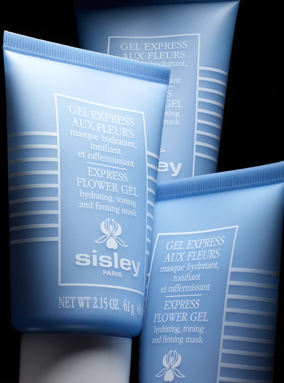 Three Sisley Gel Express Aux Fleurs hydrating and toning face masks in light blue tubes, arranged on a black surface in a studio setting.