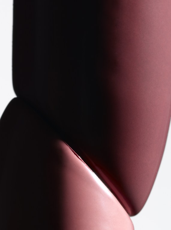 Close-up shot of a modern cosmetic container with a sleek, curved design in a reddish-pink hue against a bright white background.