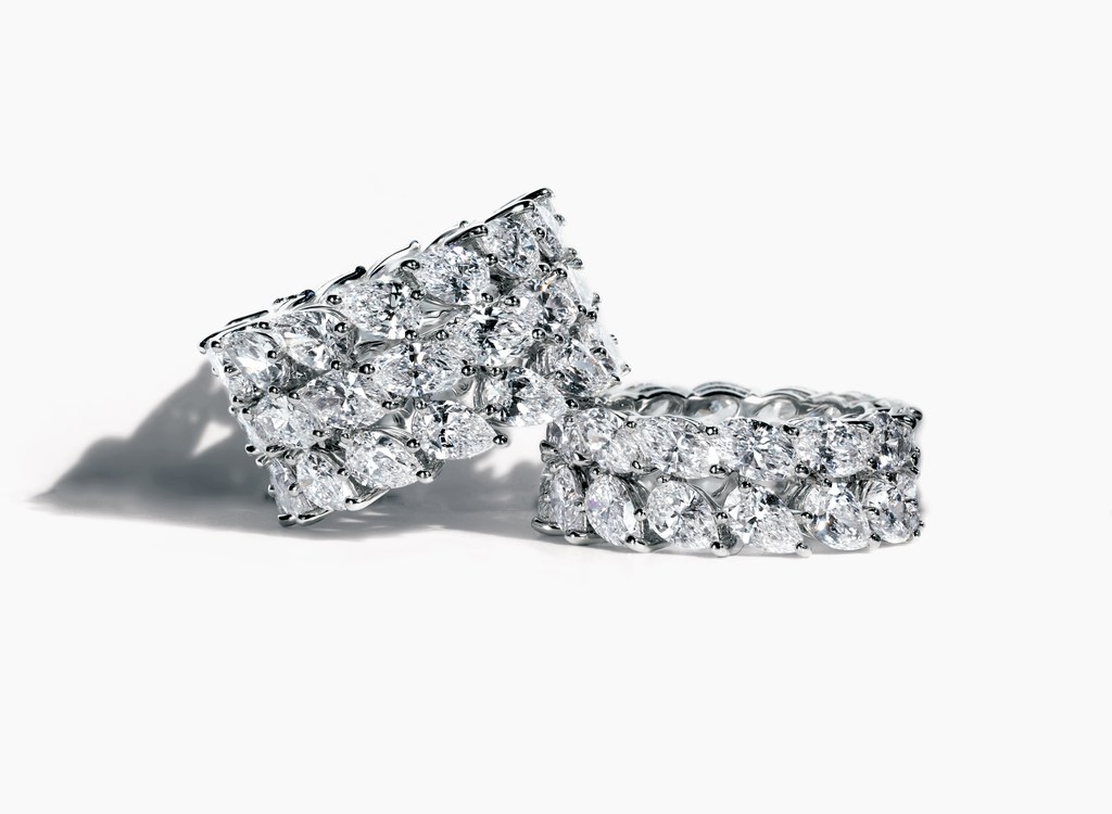 Two diamond eternity bands are stacked on a white surface. The bands have multiple pear-shaped diamonds set in a repeating pattern.