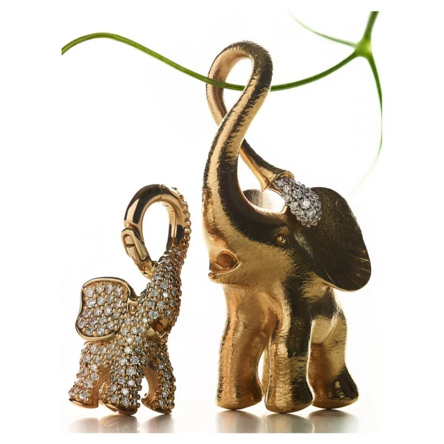 Elevated close-up captures two ornate golden elephant figurines adorned with diamonds, complemented by a gracefully curving green plant stem.