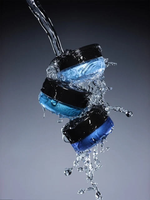 Three black jars with blue cream under a stream of splashing water, product shot for beauty or cosmetic advertising.