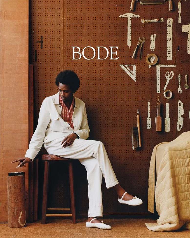A person wearing a white jacket and pants sits on a stool in front of a pegboard wall displaying tools in an indoor setting.