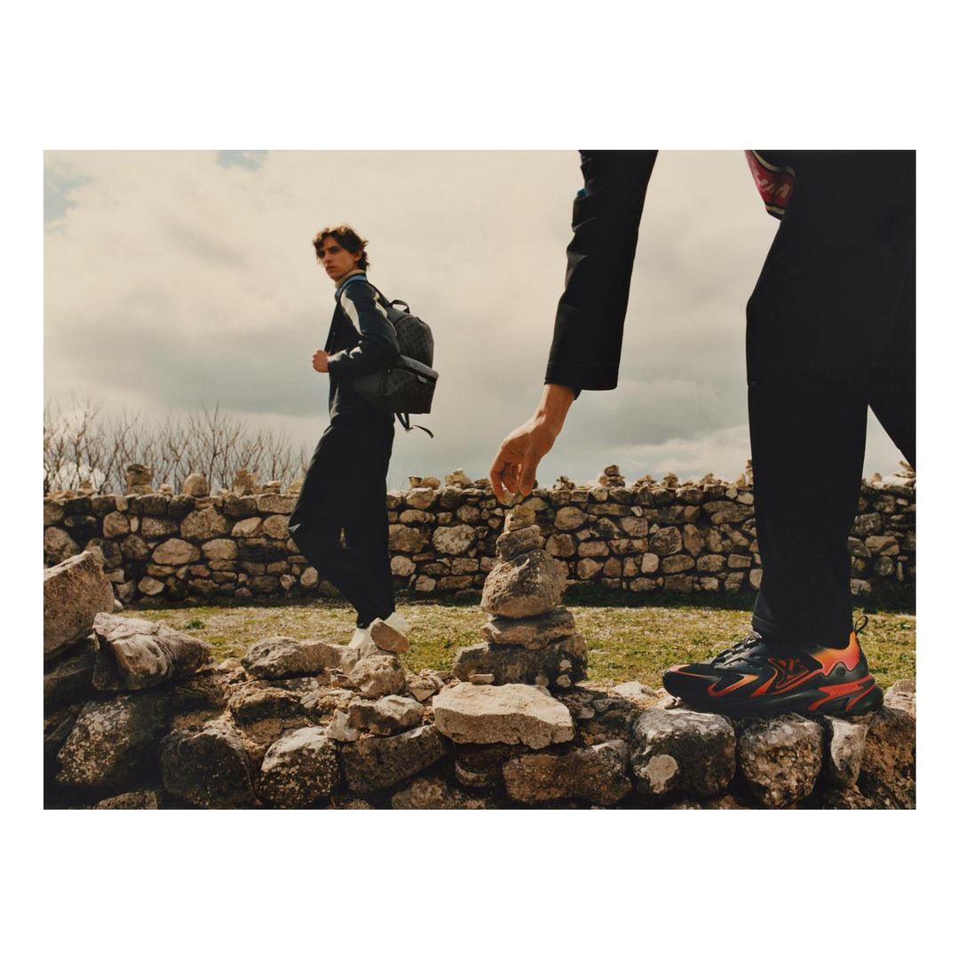 Two people on a rocky hillside with stone walls, one stacking rocks, the other wearing a backpack and looking back on the trail.