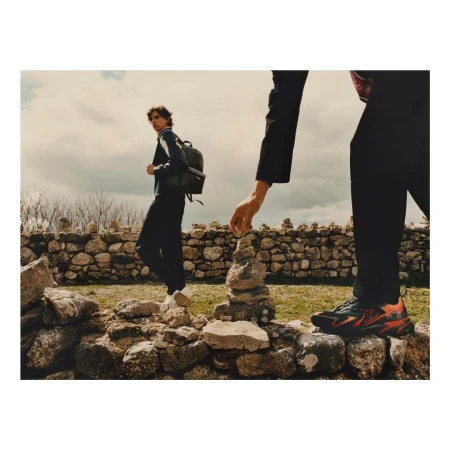 Two people on a rocky hillside with stone walls, one stacking rocks, the other wearing a backpack and looking back on the trail.