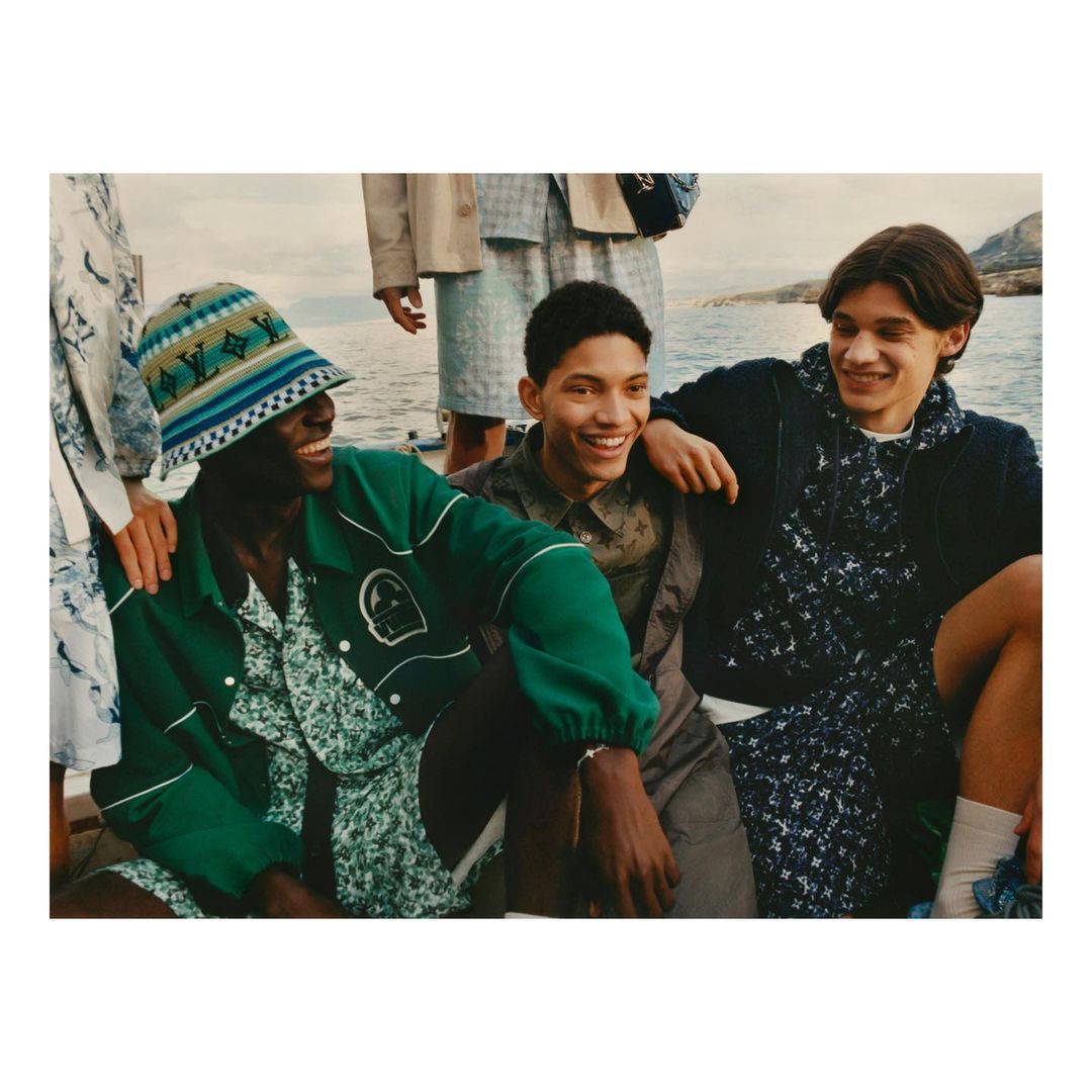 Group of young men wearing casual summer clothing and hats pose outdoors near water for a fashion editorial.