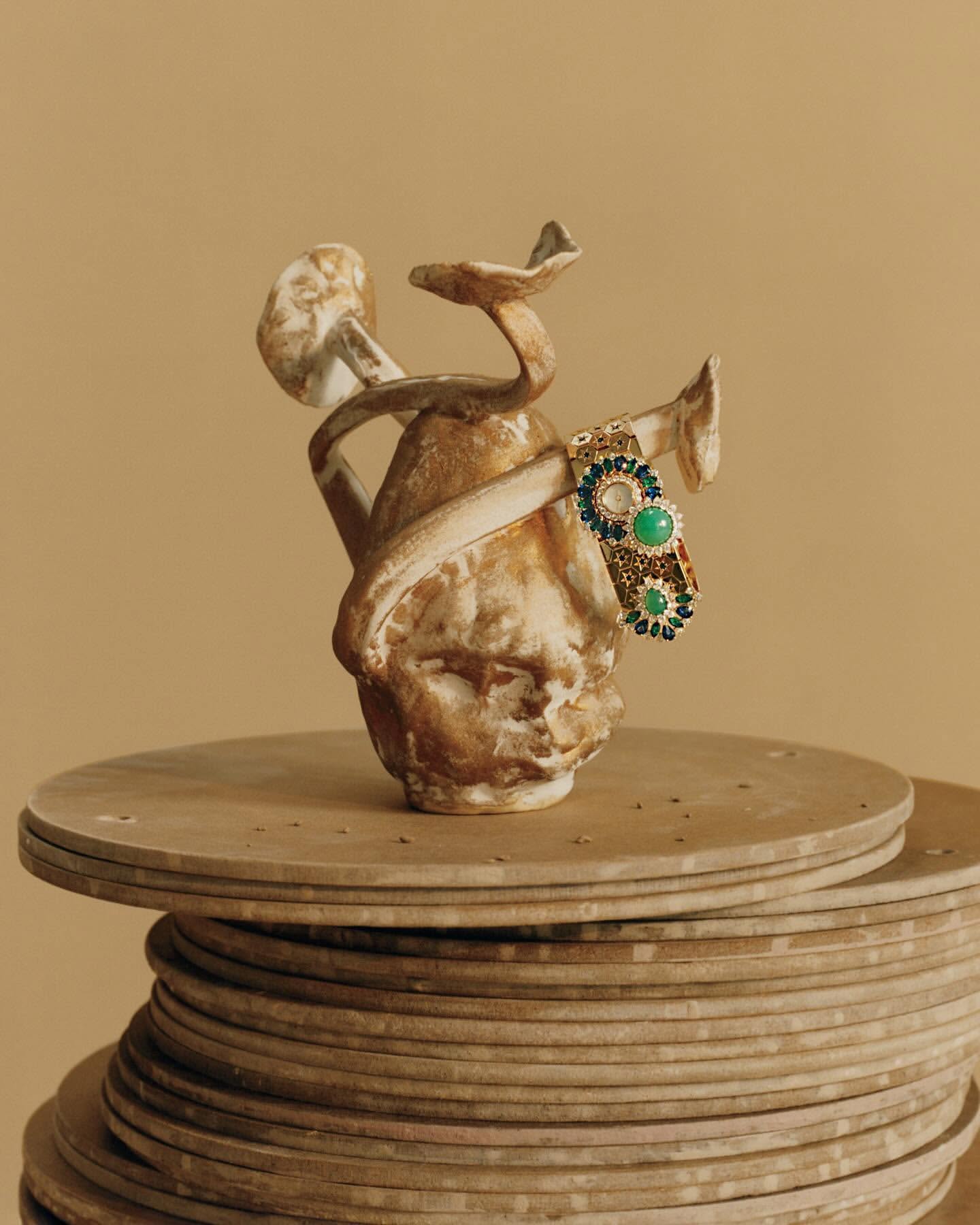 Still life shot of a ceramic head sculpture with mushroom-like growths adorned with a jeweled bracelet sitting on a tiered base.