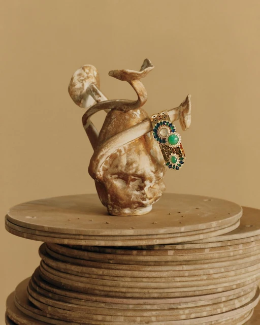 Still life shot of a ceramic head sculpture with mushroom-like growths adorned with a jeweled bracelet sitting on a tiered base.