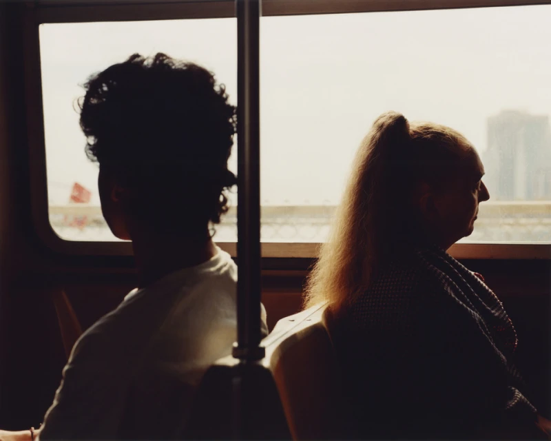 Silhouetted view of two people riding public transportation. The individuals look out windows on a city trip with a cityscape backdrop.