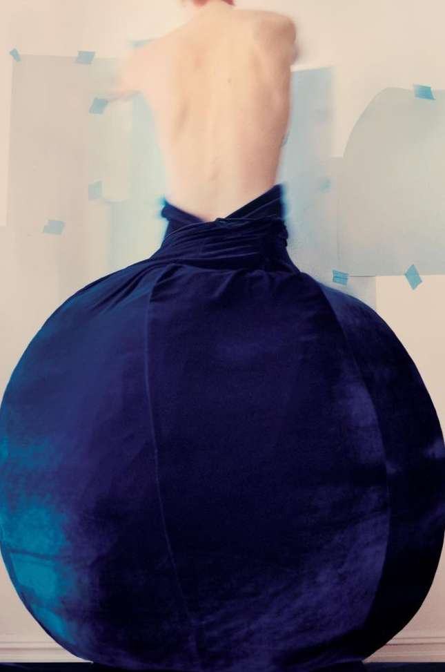 Person wearing a large, spherical navy blue dress in a studio. The dress dominates the frame, with the person's bare back visible.