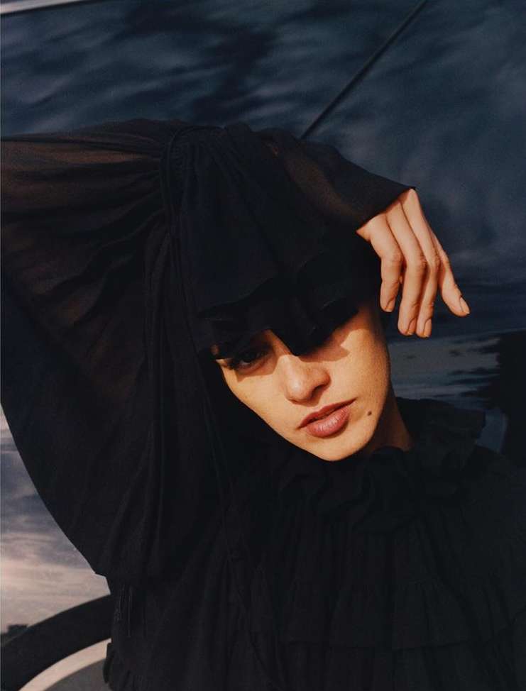 Close-up portrait of a young adult female wearing a black ruffled blouse with soft, diffused light and a muted blue background.