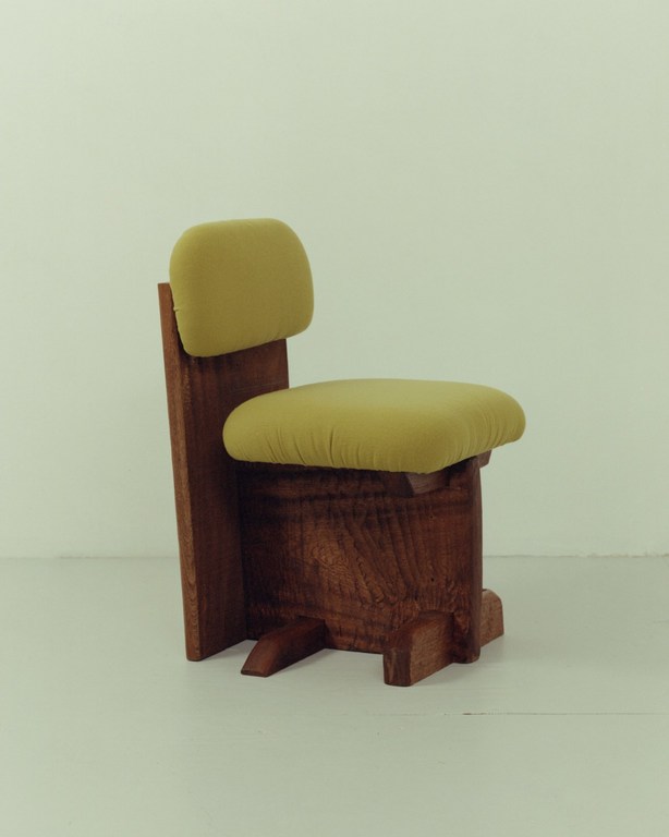 Wooden chair with a cushioned seat and backrest in pale yellow set against a neutral backdrop, showcasing its design and craftsmanship.