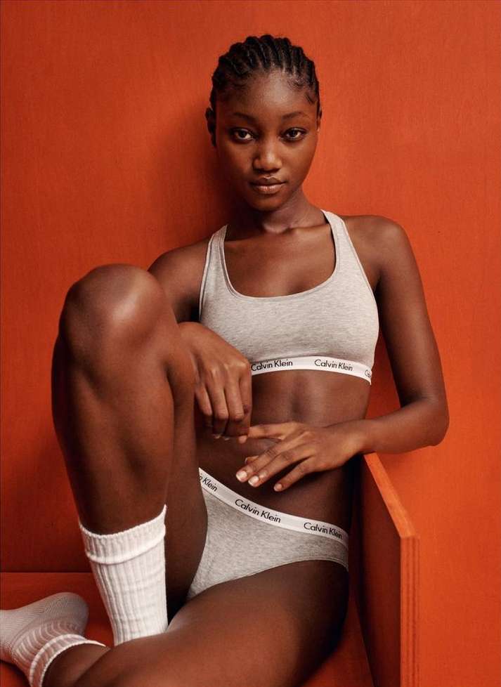 Black woman in grey Calvin Klein underwear and white socks seated against a warm terracotta orange background