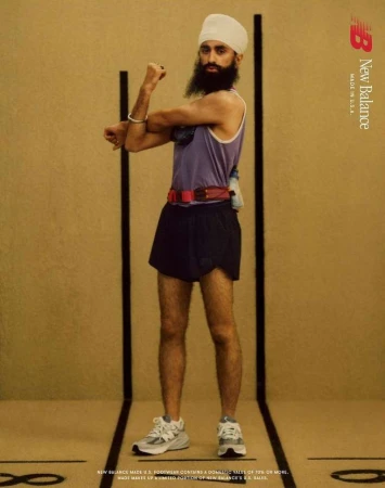 An adult male wearing athletic shorts, a tank top, and New Balance running shoes poses in a studio with a tan background for an advertisement.