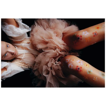 Overhead shot of a woman in a tulle dress with flower body art lying against a black background, creating a surreal and visually striking image.