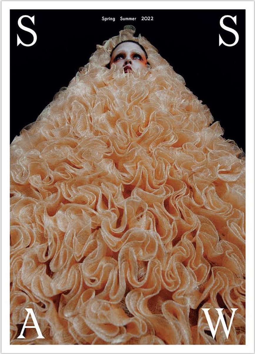 High fashion magazine cover featuring a model in an enormous, light orange ruffled dress against a black background with bold white text.