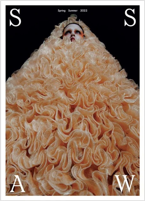 High fashion magazine cover featuring a model in an enormous, light orange ruffled dress against a black background with bold white text.