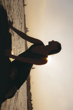 Silhouette of a woman seated on a boat against a bright sunset sky reflecting on water