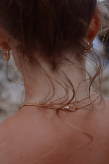 Close-up from behind of an adult female wearing a gold necklace and hoop earrings, with soft lighting and focus on the jewelry details.