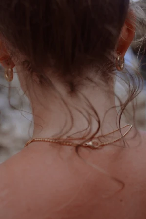 Close-up from behind of an adult female wearing a gold necklace and hoop earrings, with soft lighting and focus on the jewelry details.