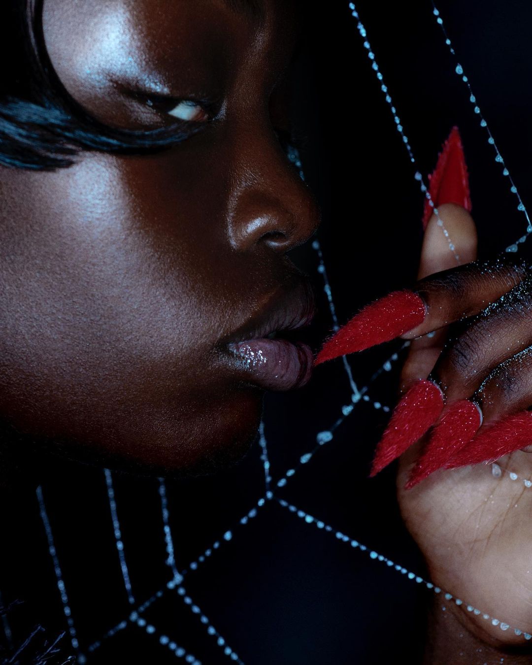 Close-up of an adult woman with dark skin and bright red fingernails, striking pose, dark background, dramatic beauty.