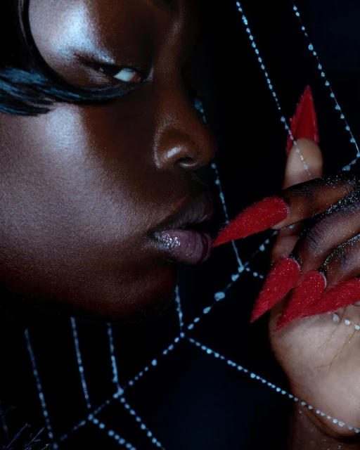 Close-up of an adult woman with dark skin and bright red fingernails, striking pose, dark background, dramatic beauty.