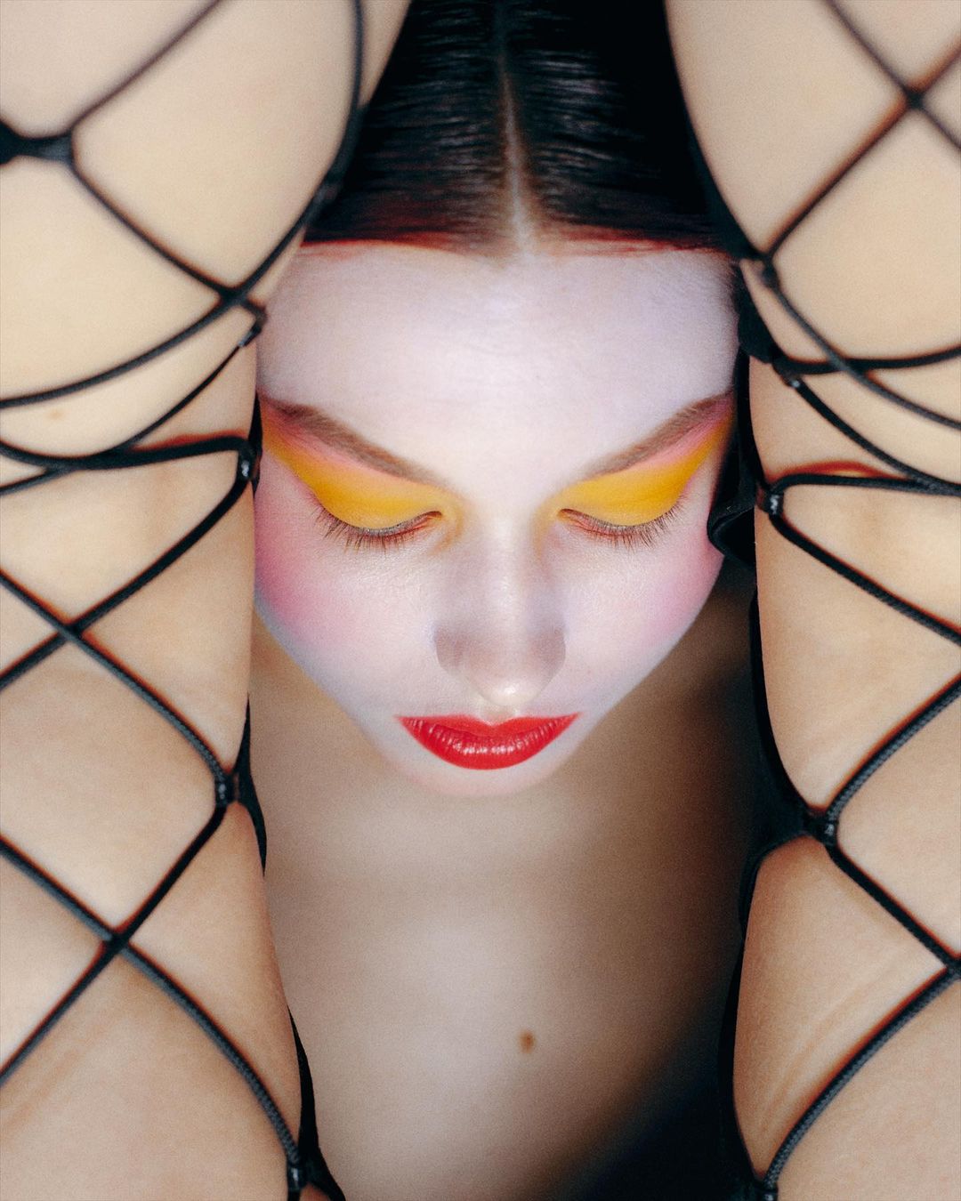 Close-up portrait of a woman with vibrant yellow eye shadow framed by legs in black lace-up fishnet stockings