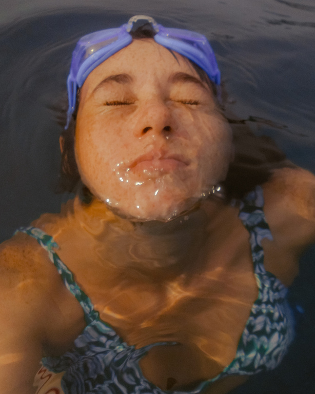 A woman with goggles floats in clear water, eyes closed, showcasing a peaceful and relaxed moment in a natural setting.