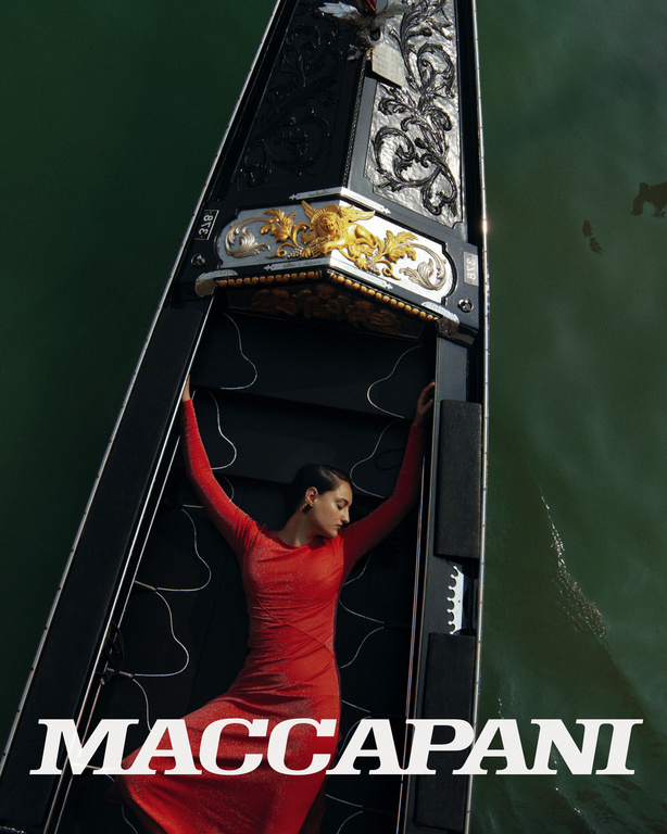 Aerial view of a woman in a red dress reclining in a gondola on the water, creating a striking and elegant composition.