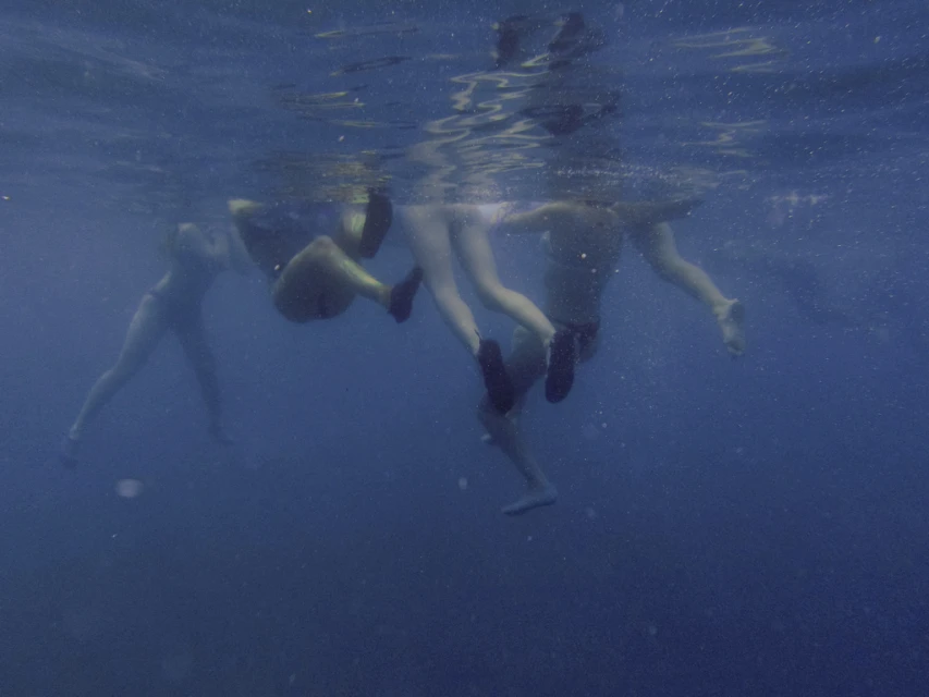 Underwater view of four people swimming in a clear, blue ocean, captured with a wide angle, showcasing their figures against the water.
