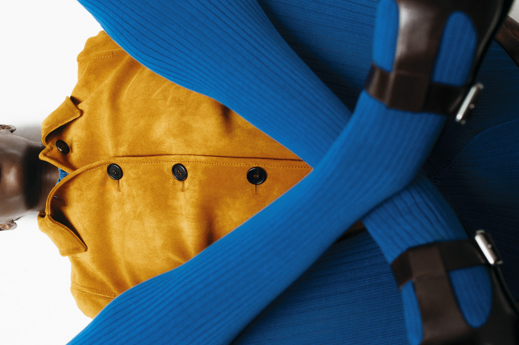 An eye-level shot features a Black model wearing a mustard jacket, blue ribbed top and leggings, and brown heeled Mary Jane shoes on white.