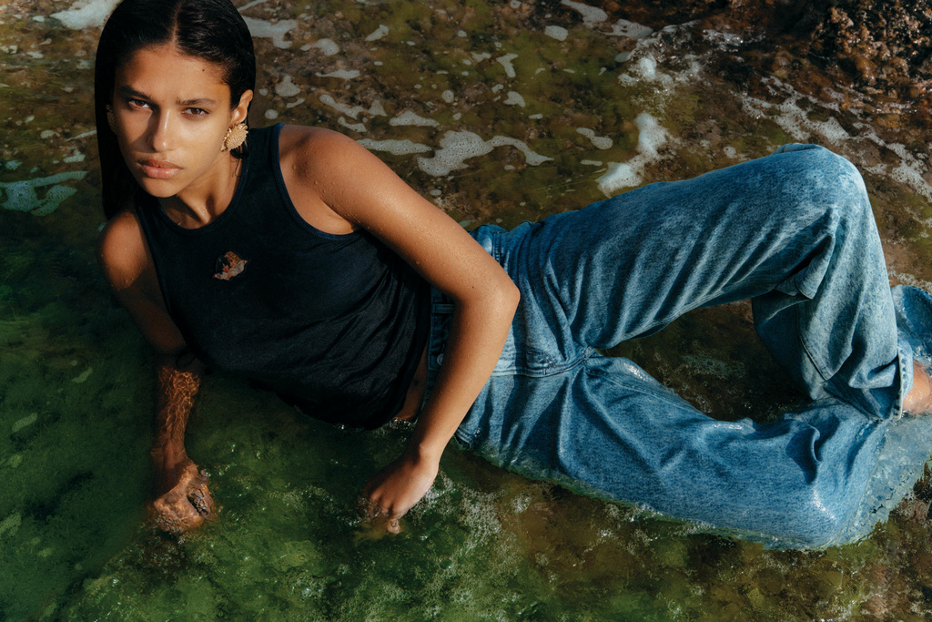 Woman poses in water wearing a black tank top and jeans. The close-up shot captures her lounging in a natural, aquatic environment.