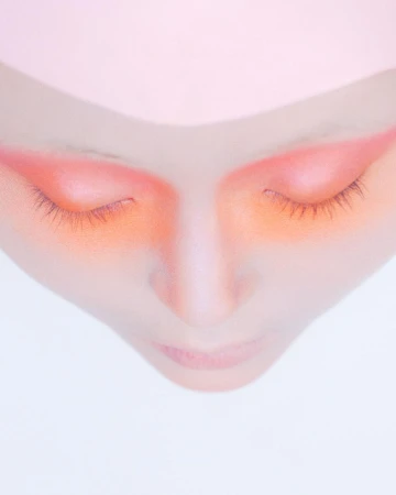 Close-up overhead portrait of a person with peach eyeshadow and closed eyes against a white background