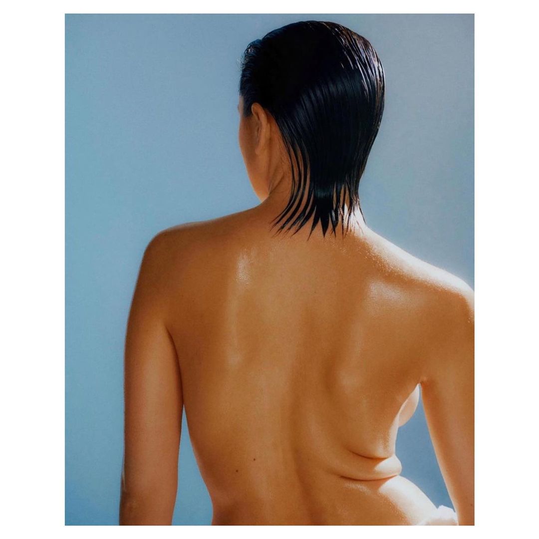 Back view portrait of a person with wet, dark hair against a light blue backdrop in a photo studio showcasing beauty and wellness.