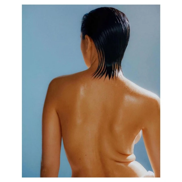 Back view portrait of a person with wet, dark hair against a light blue backdrop in a photo studio showcasing beauty and wellness.
