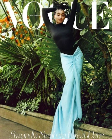 Vogue cover featuring Amandla Stenberg in a black top and draped blue skirt, posing amid lush greenery and foliage.