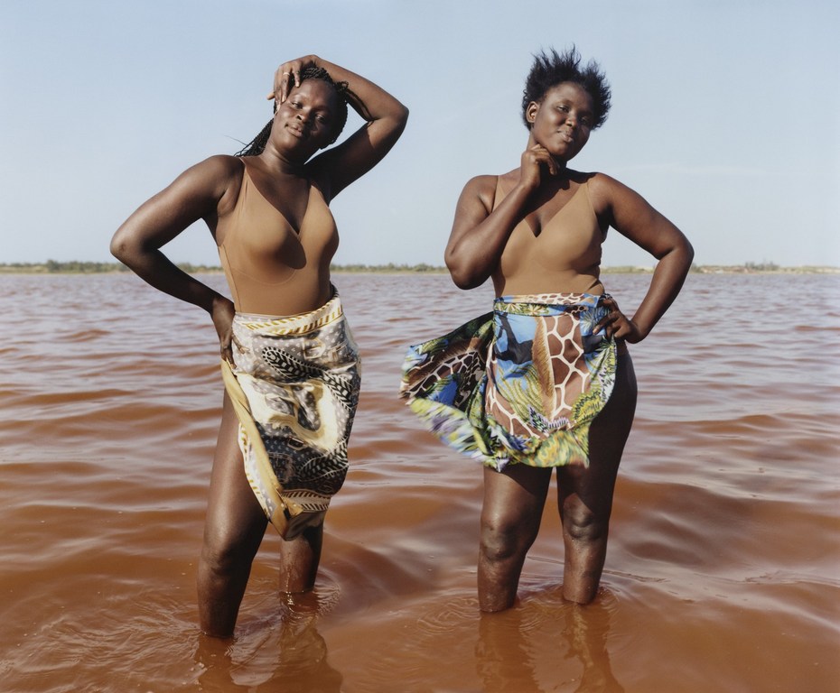 Two African women in swimwear stand in the Rose Lake of Senegal, West Africa, wearing sarongs, enjoying the warm water and clear sky.