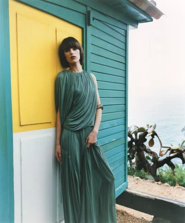 Woman in a green pleated dress leaning against a turquoise and yellow wooden beach cabin photographed by Markn.