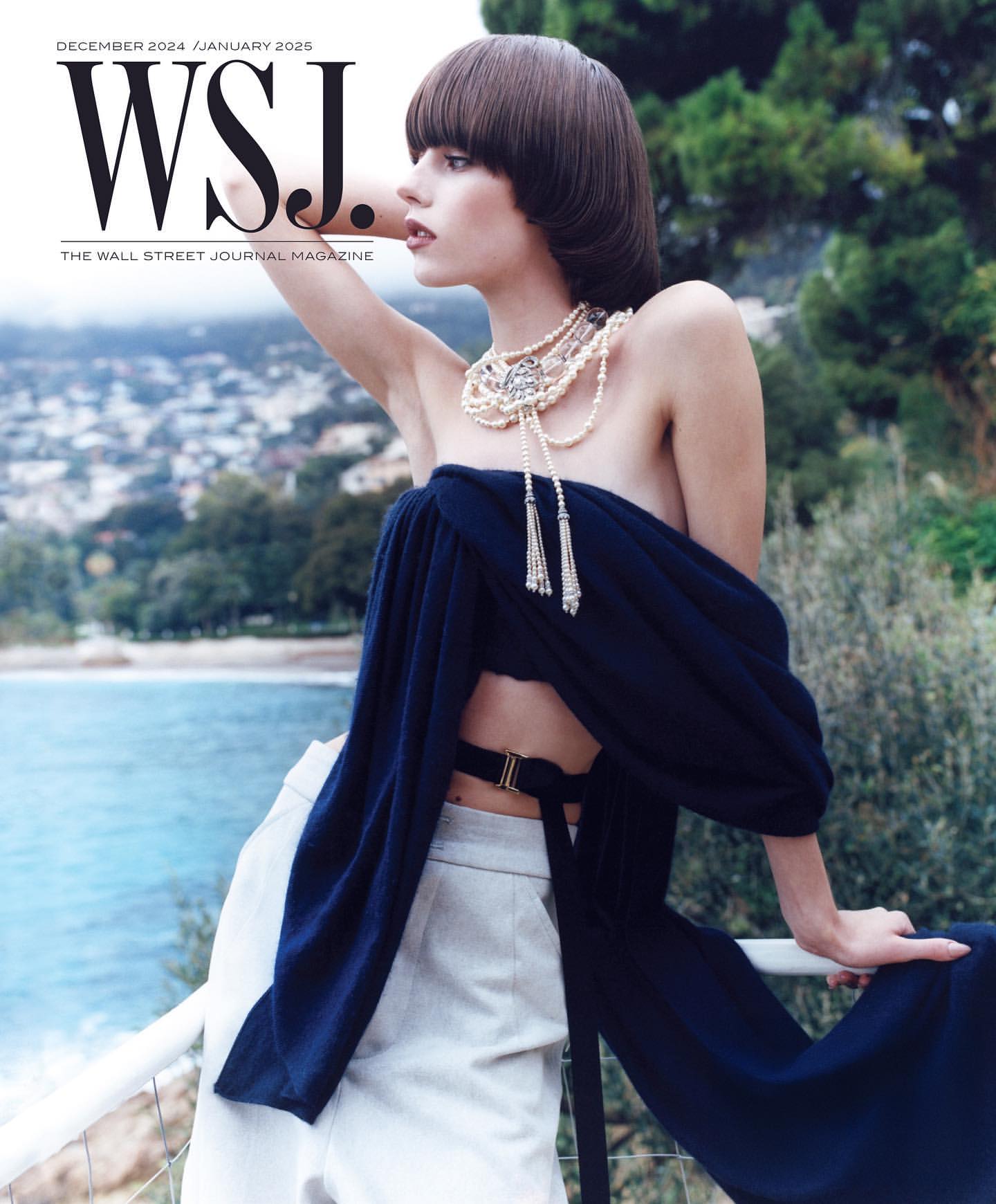 Magazine cover shot of a woman with a blunt bob haircut wearing a dark blue top and pearl necklace with an ocean background.