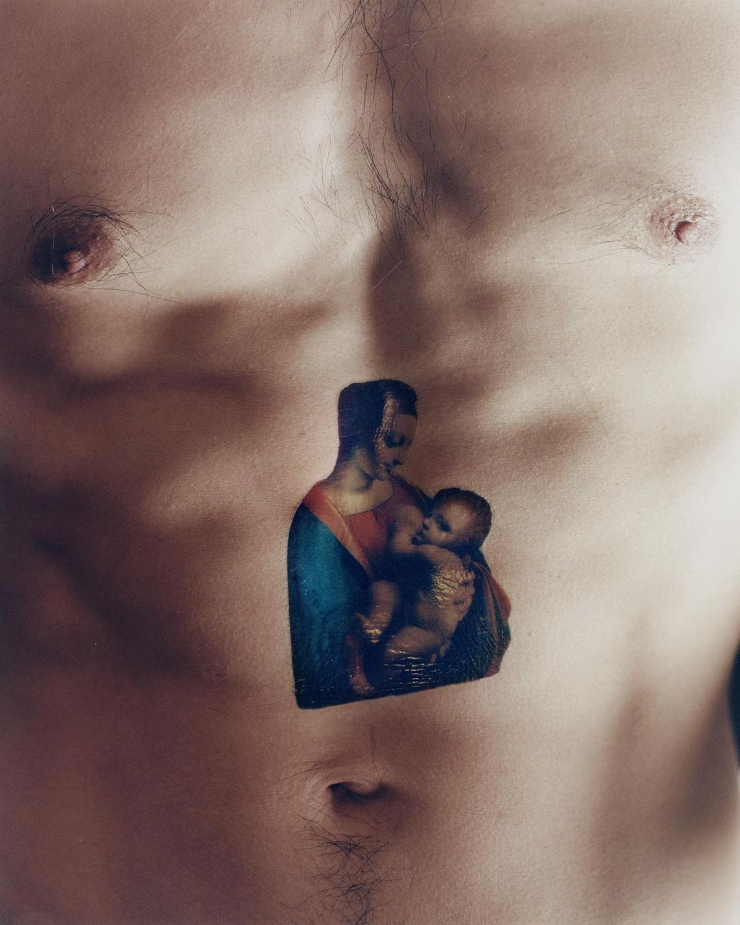 Close-up of bare male chest with a tattoo of Madonna and Child in the center. Body hair is visible. Skin tone is fair.