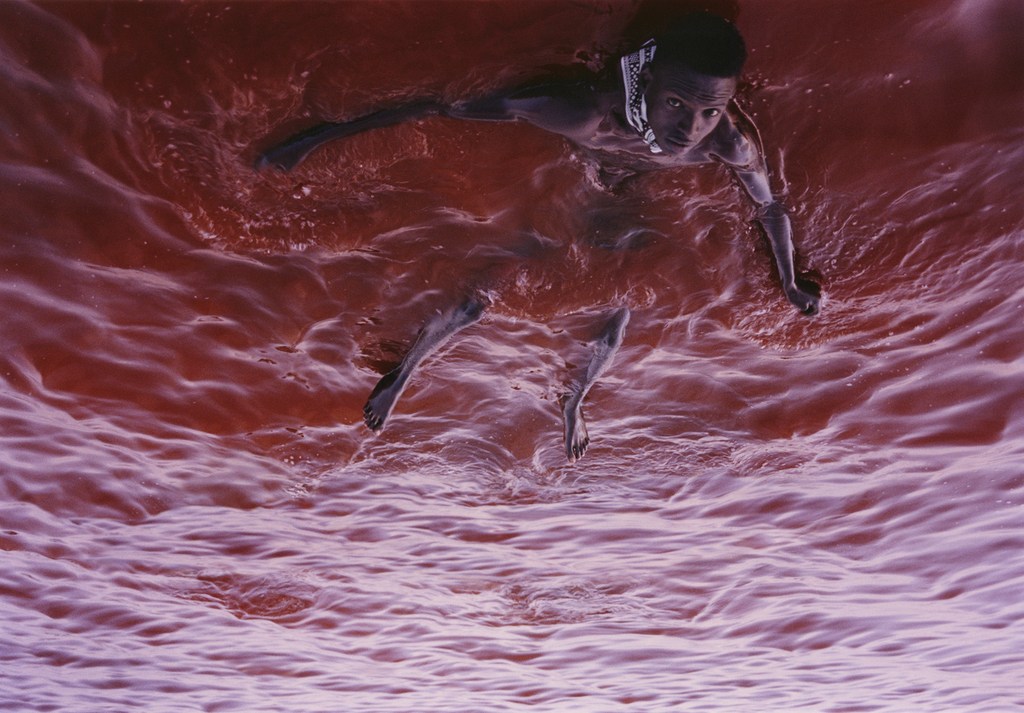Artistic shot of an adult male swimming in deep pink water, captured with an eye-level angle and soft lighting. A unique visual.